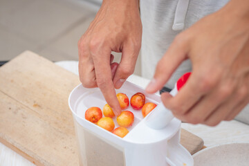 Worker uses a simple tool to extract pits from fresh cherries and prepare them for further use. Manual work with fruit. Seasonal work