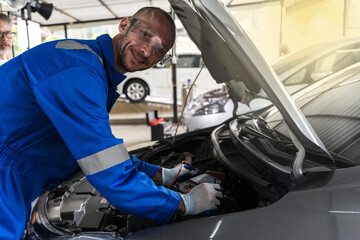 Smiling Caucasian car mechanic man working with openhooded vehicle in auto repair, Car Mechanic