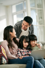 young asian couple and two children using laptop computer together at home