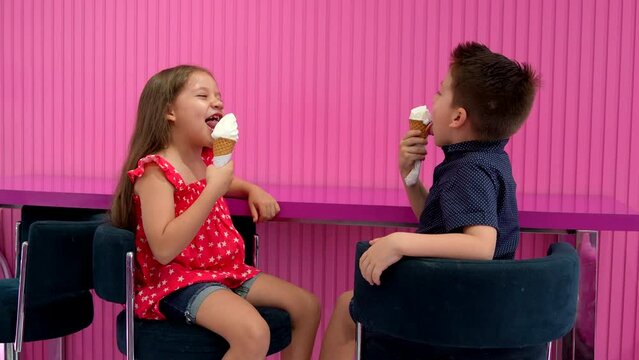Niños rubios hermanos amigos comiendo y disfrutando de un delicioso y rico helado nieve para el calor en un fondo rosa en la heladería alegres y contentos muy felices saboreando una rica nieve en cono