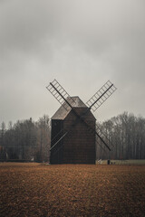 Fototapeta na wymiar Ancient wooden mill standing alone in a field in gloomy foggy weather. Historical building for grinding corn, Opava, Czech Republic