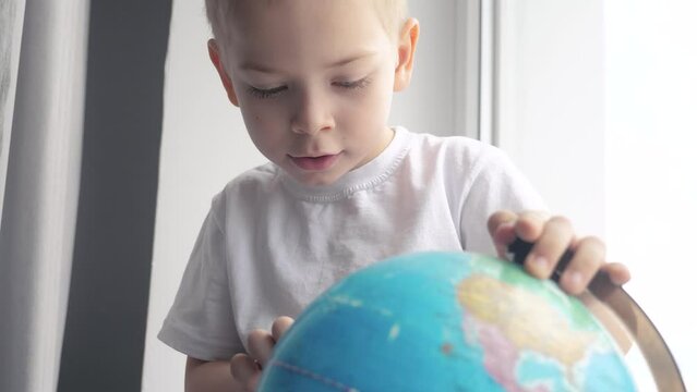 boy studies globe. education travel tourism concept lifestyle. child twists the globe sits on a window sill. kid looking for a country on a globe map. world map geography study