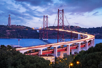 View of Lisbon view from Miradouro do Bairro do Alvito viewpoint of Tagus river, traffic with light trails on 25th of April Bridge, and Christ the King statue in the evening twilight. Lisbon, Portugal