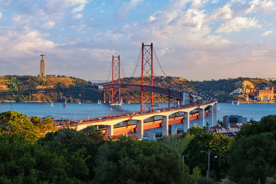 View of Lisbon view from Miradouro do Bairro do Alvito tourist viewpoint of Tagus river, traffic on 25th of April Bridge, and Christ the King statue at sunset. Lisbon, Portugal
