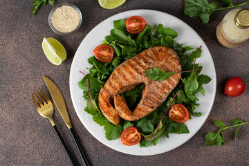 Baked salmon steak served with arugula and cherry tomatoes on a white plate