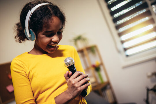 Cute preteen black girl holding a microphone singing karaoke at home, recording songs for a contest. Children's lifestyle concept