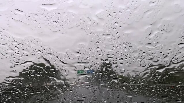 Raindrops falling over windscreen car glass while driving on highway with wiper cleaning