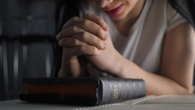 girl praying indoors at bedtime on bible. religion concept evening prayer woman brunette hands on bible praying by bed lifestyle