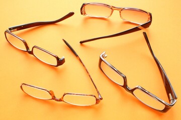 Old broken eyeglasses with damaged legs on yellow background. Poor eyesight. Reuse and repair...