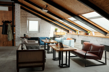 Interior of spacious loft studio or coworking space with tables in the center surrounded by several stylish and comfortable couches and armchair