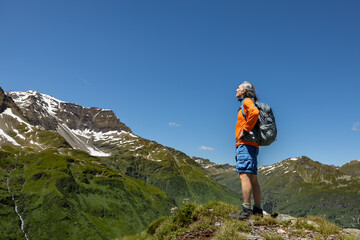 Adult male hiker with backpack standing at a height and looking at a mountain landscape with snow-capped peaks, Austria