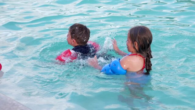 Ni&ntilde;os hermanos primos amigos latinos y rubios hispanos jugando divertidos nadando en el verano en una alberca o piscina en agua salpicando y disfrutando de una tarde soleada al aire libre 
