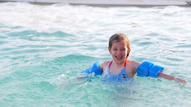 Niña rubia  hispana feliz aprendiendo a nadar en la piscina en la alberca al aire libre de un día soleado disfrutando y divertida flotando y saltando en el agua en el verano cálido