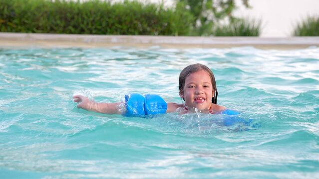 Niña rubia latina hispana feliz nadando en la piscina en la alberca al aire libre una tarde de un día soleado disfrutando y divertida flotando y saltando en el agua en el verano