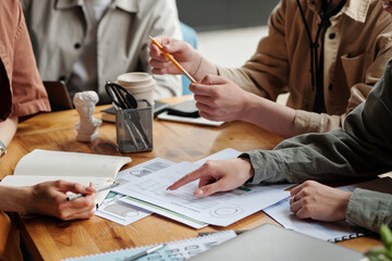 Hand of young female economist pointing at financial document and explaining data to colleagues...