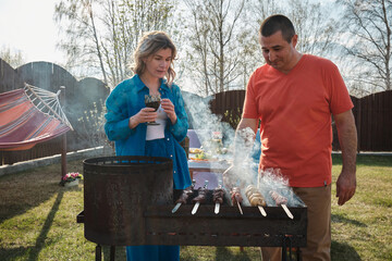 Man and woman couple grilling meat together in backyard at home for dinner, smoke from the meat