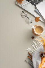Cozy autumn office design. Top vertical view of laptop, freshly cup of beverage, diaries, reading glasses, cozy checkered blanket, yellow, orange leaves on grey backdrop with space for text or ad