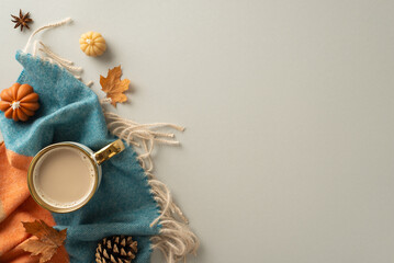 Capture the essence of homey autumn comfort with this above view photo. Hot coffee, patchy scarf, pumpkin candles and maple leaves on grey backdrop provide inviting atmosphere for text or advert