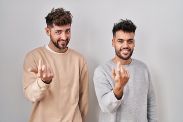 Young homosexual couple standing over white background beckoning come here gesture with hand inviting welcoming happy and smiling