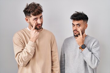 Young homosexual couple standing over white background pointing to the eye watching you gesture, suspicious expression