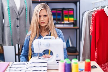 Blonde woman dressmaker designer using sew machine skeptic and nervous, frowning upset because of problem. negative person.