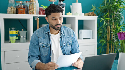 African american man using laptop reading document looking upset at dinning room