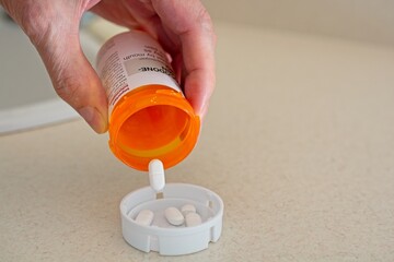 Hand held prescription bottle with pill dropping into cap on countertop
