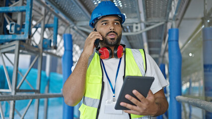 African american man builder talking on smartphone using touchpad at street