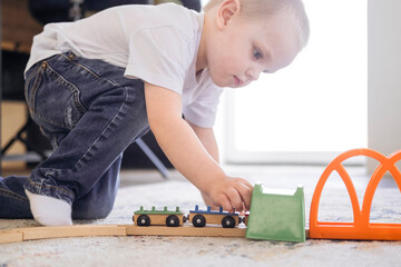 A little boy rides trains on the railroad at home on the floor. The kid spends time playing.