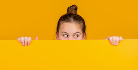 teen girl hiding behind blank yellow paper with copy space for advertisement