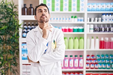 Handsome hispanic man working at pharmacy drugstore thinking concentrated about doubt with finger...