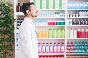 Handsome hispanic man working at pharmacy drugstore looking to side, relax profile pose with natural face and confident smile.