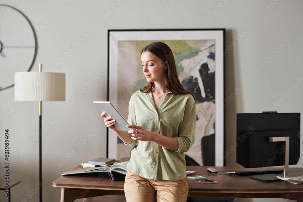 Poster young confident businesswoman with table looking through data on screen while standing in front of c