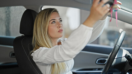 Fototapeta na wymiar Young blonde woman setting rear view mirror at street
