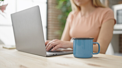 Young blonde woman using laptop sitting on table at dinning room