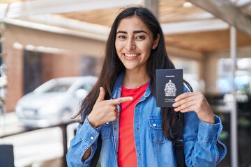 Young teenager girl holding canada passport smiling happy pointing with hand and finger