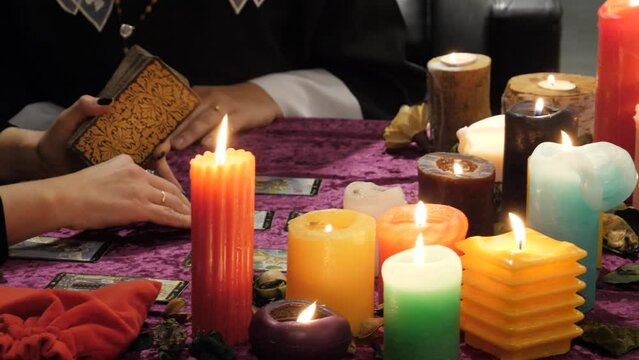 Tarot reader holds cards and reads the future, good luck. Occultism, esotericism, divination, witchcraft. Unrecognizable predictor of future, table with multi-colored candles, atmosphere of mysticism