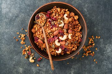 Obraz na płótnie Canvas Homemade granola with greek yogurt or milk and cashews, almonds, pumpkin with dried cranberry seeds in old bowl on dark table background. Healthy energy breakfast or snack. Top view.