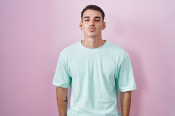 Handsome hispanic man standing over pink background looking at the camera blowing a kiss on air being lovely and sexy. love expression.