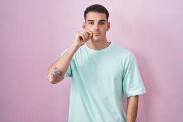 Handsome hispanic man standing over pink background mouth and lips shut as zip with fingers. secret and silent, taboo talking