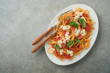 Salad caprese or pasta spaghetti broken with basil and mozzarella ala caprese on white plate on grey rustic concrete background. Traditional Italian cuisine. Italian food concept.  Top view. Recipe.