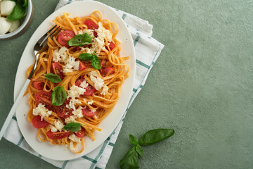 Salad caprese or pasta spaghetti broken with basil and mozzarella ala caprese on white plate on green rustic wooden background. Traditional Italian cuisine. Italian food concept. Top view. Recipe.
