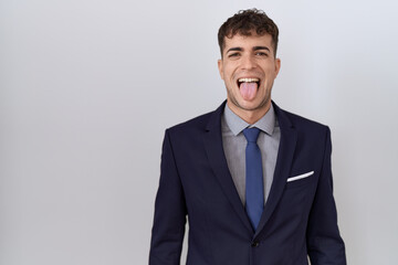 Young hispanic business man wearing suit and tie sticking tongue out happy with funny expression. emotion concept.