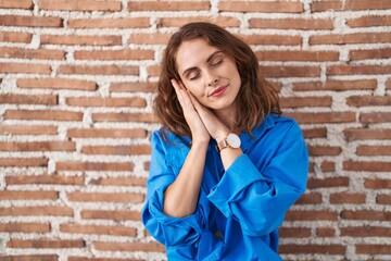Beautiful brunette woman standing over bricks wall sleeping tired dreaming and posing with hands together while smiling with closed eyes.