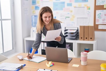Young blonde woman business worker reading document writing on notebook at office