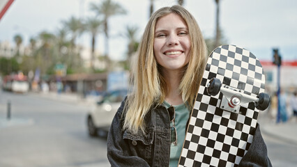 Fototapeta premium Young blonde woman smiling confident holding skate at street