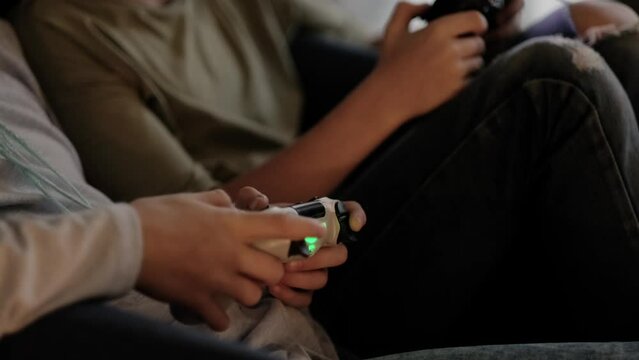 kids hands with joysticks, two children siblings playing video game console while sitting at home, real people, leisure concept.