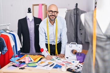 Young bald man tailor smiling confident drawing clothing design at tailor shop