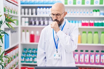 Hispanic man with tattoos working at pharmacy drugstore feeling unwell and coughing as symptom for...