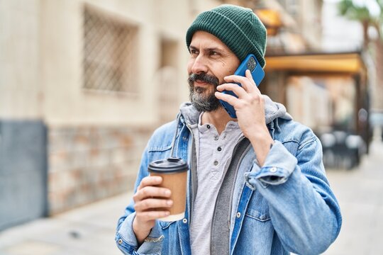 Young bald man talking on smartphone drinking coffee at street